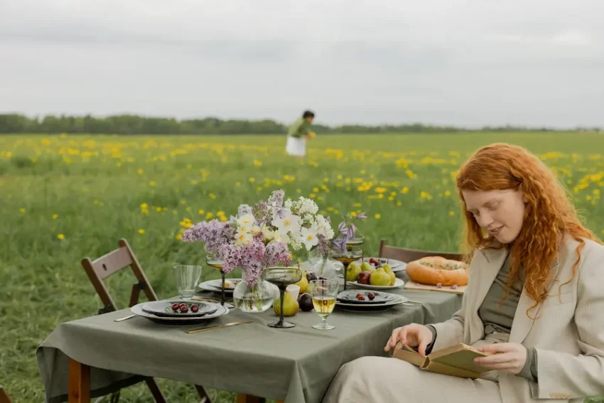 mujer peliroja leyendo en el campo con mesa desayuno